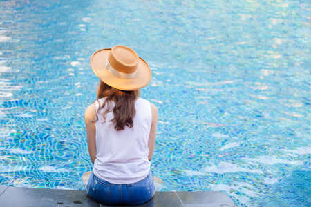 Young beautiful woman with hat sitting at the pool. Asian girl relaxing in swimming pool. Happiness lifestyle conceptsの写真素材