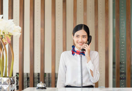 Young woman receptionist talking on the phone at workplace, Portrait of Female receptionist working in hotelの写真素材