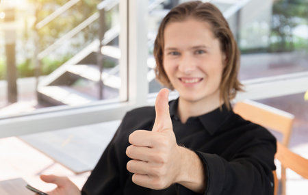 Smiling man giving thumbs up and holding smartphone blurred backgroundの写真素材
