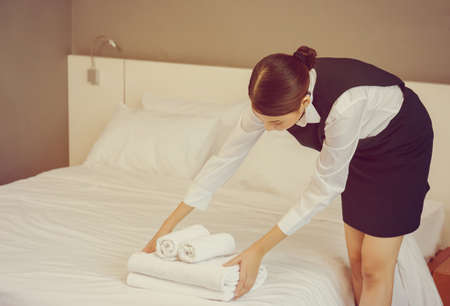 Room service putting stack of fresh white bath towels on the bed sheet. Female housekeeper putting clean towels on bed. Room service maid cleaning hotel room.の写真素材
