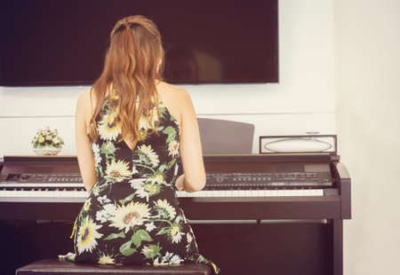 Rear view of Beautiful woman in dress playing piano, Young girl playing grand piano at homeの写真素材