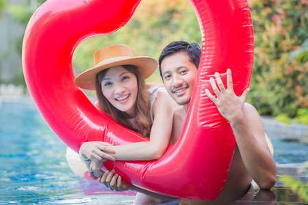 Cheerful young friends having fun in heart shaped inflatable, Happy young couple having fun at swimming pool. Happiness lifestyle conceptsの写真素材