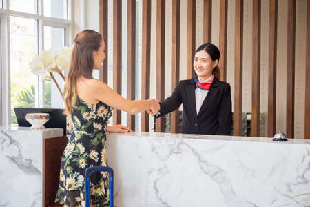 Happy receptionist and guest making handshake at hotel reception, receptionist standing at hotel counter with young female travellersの写真素材