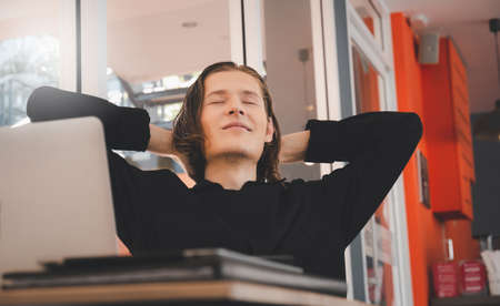Relaxed young male sit at desk distracted from computer work take break, man sit relax at office workplace take nap or daydreamingの写真素材