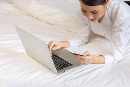 Young woman shopping online with credit card and laptop computer on bed. Women doing online shopping on the bed.の写真素材