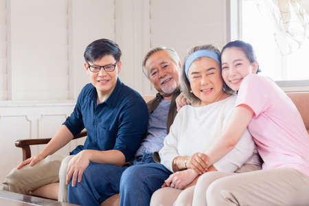 Cheerful Asian family in living room, Senior father mother and middle aged son and daughter sitting on sofa looking at camera, Happiness family conceptsの写真素材