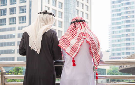 Rear view of two arab middle eastern standing outside in the city, two muslim business man waering traditional clothes standing outdoor city backgroundの写真素材