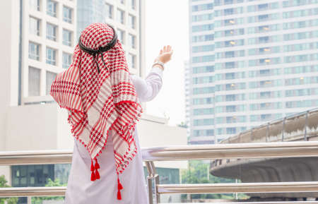 Rear view of young business arab middle eastern muslim man standing while raised hands and praying in cityの写真素材
