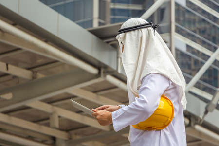 Arab Middle Eastern architect holding yellow helmet and checking tablet PC in downtownの写真素材