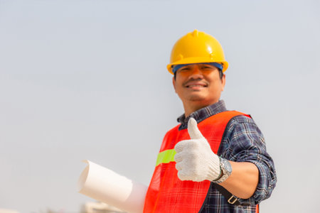 Smiling engineer, worker man holding blueprint with giving thumb up at construction site