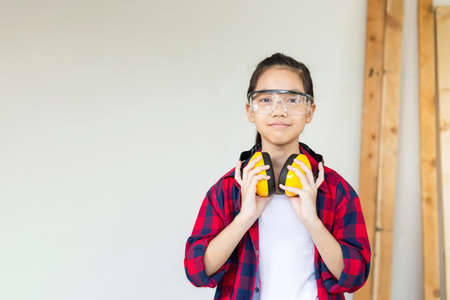 Happy girl standing with noise reduction earmuffs in a carpentry workshop. Children learning woodworking in the craftsman workshopの写真素材