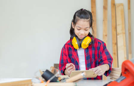 Happy girl standing with noise reduction earmuffs in a carpentry workshop. Children learning in the craftsman workshopの写真素材