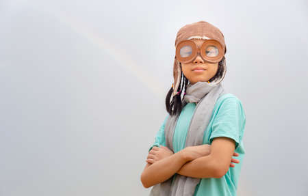 Asian child girl in the old style pilot uniform stands with arms crossed, Happy kid playing outdoorsの写真素材