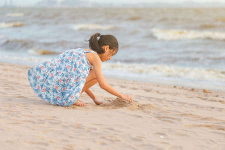 Kid play with sand on the beach, Little girl playing outdoor sunset evening timeの写真素材