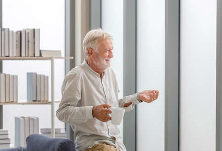 Senior man inside new home during a coffee break, Elderly man standing near window with cups of coffeeの写真素材