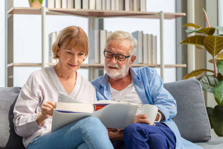 Portrait of happy senior couple in living room, Elderly woman and a man reading a book on cozy sofa at home, Happy family conceptsの写真素材