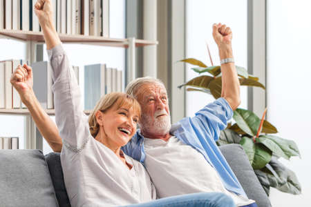 Portrait of happy senior couple cheer on their favorite team while watching football game in living room, Elderly woman and a man relaxing on cozy sofa at home, Happy family conceptsの写真素材