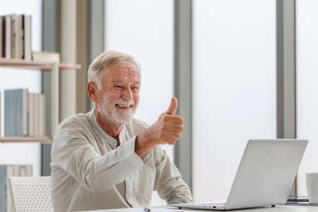 Portrait of senior man using laptop using laptop talking on video call at home, Happy senior man in living room with laptop computer gadgetの写真素材