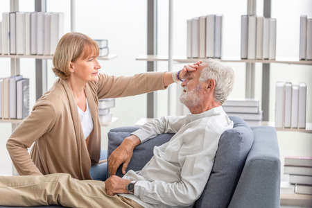 Woman checking fever on forehead by hand, Elderly woman touches the forehead of old husband, Senior couple and happy family conceptsの写真素材