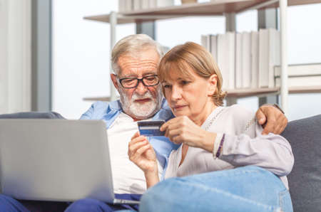 Portrait of happy senior couple shopping online in living room, Elderly woman and a man using computer laptop on cozy sofa at home, Happy family conceptsの写真素材