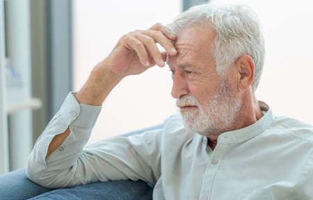 Thinking senior man sit on couch in living room, man thinks and sit on the sofaの写真素材