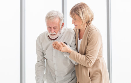 Senior man is having back pain and his attractive old woman supports him. Elderly man suffering from back pain and takes care by his wifeの写真素材