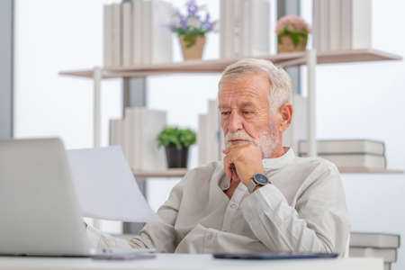 Worried senior man checking their bills, retired elderly old family reading documents, Mature man in living room with laptopの写真素材