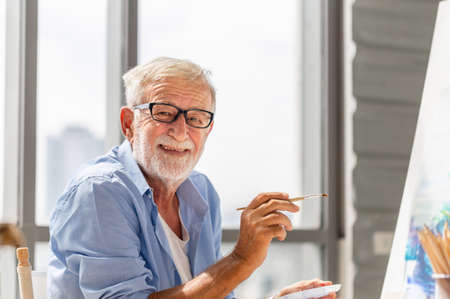Elderly man painting on a canvas, Smiling mature man painting on canvas at home, Happy retirement conceptsの写真素材