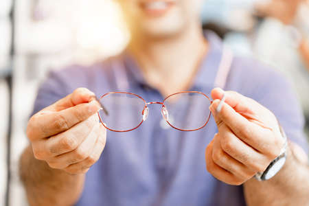 Cheerful man holding eyeglasses in optics store, happy man choosing glasses at optics shopの写真素材