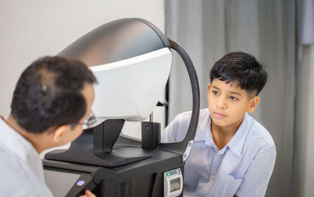 Boy doing eye test checking examination with autorefractor in optical shop, Optometrist doing sight testing for child patient, Eye doctor examinating kid patientの写真素材