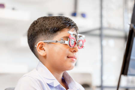 Portrait of child wearing eye test glasses in the optical shop, Smiling Indian-thai boy choosing glasses in optics storeの写真素材