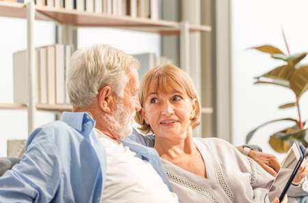 Senior couple in living room, Elderly man and a woman using tablet smartphone on cozy sofa at home, Happy family conceptsの写真素材