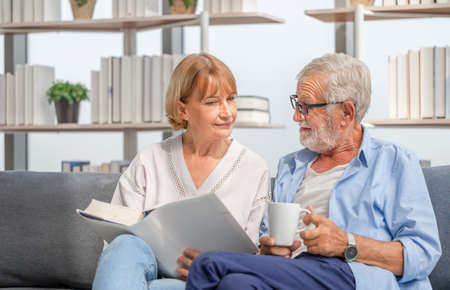 Portrait of happy senior couple in living room, Elderly woman and a man reading a book on cozy sofa at home, Happy family conceptsの写真素材