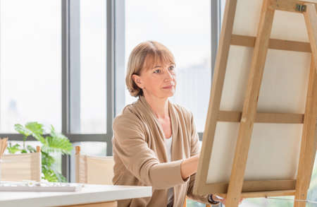 Woman painting on a canvas, Mature middle aged woman painting on canvas at home, Happy retirement conceptsの写真素材