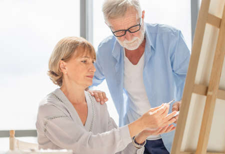 Portrait of happy senior couple painting on a canvas in living room, Older man and woman drawing together on a canvas, Happy retirement conceptsの写真素材