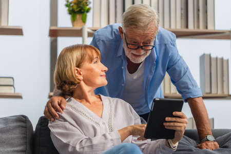 Mature woman and senior man using smartphone talking on video call on cozy sofa at home, Portrait of Cheerful senior couple in living room, Happy family conceptsの写真素材