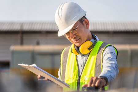 Engineer in waistcoats and hardhats with clipboard checklist inspecting construction site, Smiling...