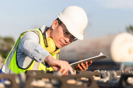 Engineer in waistcoats and hardhats with documents inspecting construction site, Mechanical worker checking of the battery storage systemの写真素材