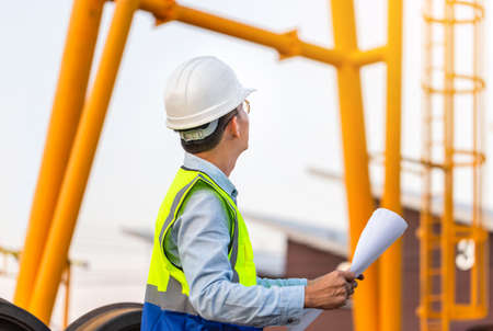 Engineer man in waistcoats and hardhats and with documents in construction site, Engineer under inspection and checking construction process railway locomotive repair plantの写真素材