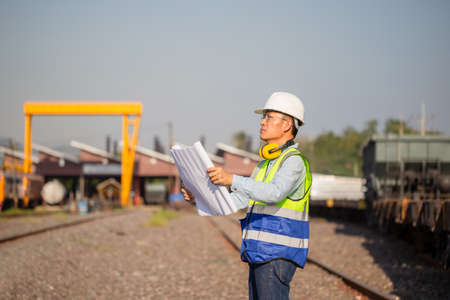 Engineer man in waistcoats and hardhats and with documents in construction site, Engineer under inspection and checking construction process railway locomotive repair plantの写真素材