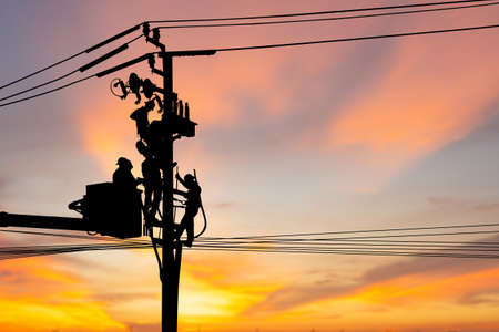 Silhouette of Electrician officer climbs a pole and uses a cable car to maintain a high voltage line system, Shadow of Electrician lineman repairman worker at climbing work on electric post power poleの写真素材