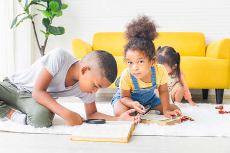 Little kid girl and boy reading book with magnifier on the floor, Happy children playing in the living roomの写真素材