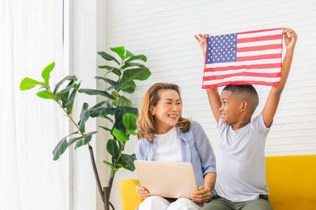 Grandmother and grandchildren playing cheerfully in living room, Woman with laptop and boy holding USA flagの写真素材