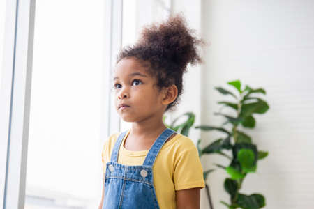 Little child girl looking outside through the window, Kid standing in living room and looking through the windowの写真素材