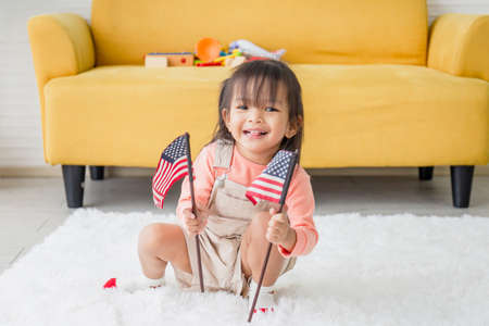 Cute little girl with a small national flag of United States, kid girl playing in living roomの写真素材