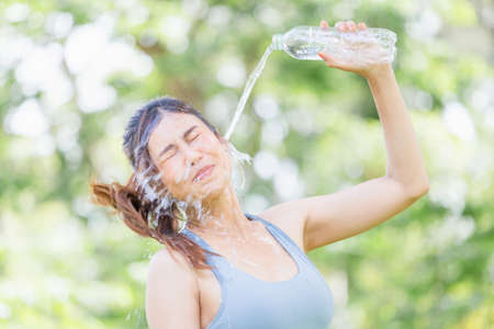 Athlete young beautiful woman drinking and splashing water in her face at summer green park, Sport woman drinking water from a plastic bottle after work out exercisingの写真素材