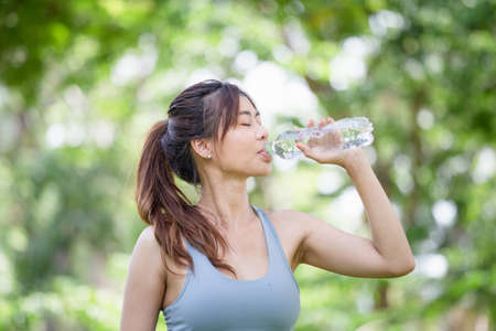 Athlete young beautiful woman drinking water from a plastic bottle at summer green park, Sport woman drinking water after work out exercisingの写真素材