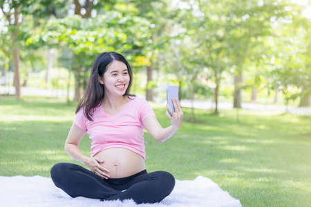 Happy pregnant woman sitting relax in the park and Virtual talking with friendsの写真素材