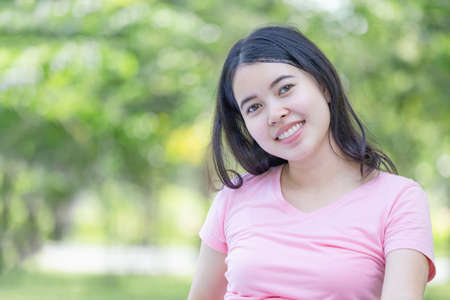 Cheerful young woman in the park, Smiling woman relax and looking at camera blurred green backgroundの写真素材