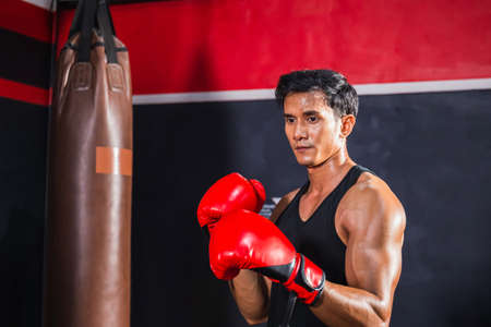 Portrait of Sportsman muay thai boxer fighting in gym, muscular handsome boxing man fighter with boxing bagの写真素材